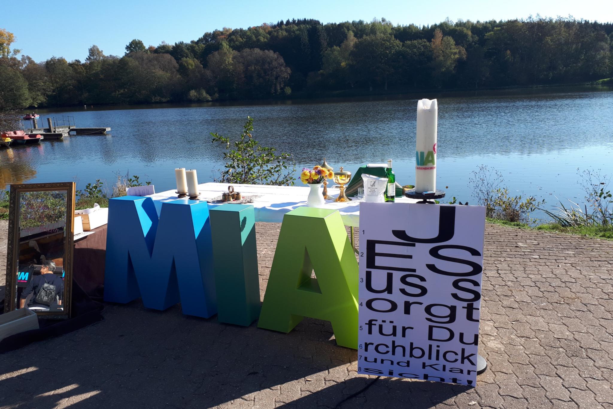 Vor einem See sieht man große Buchstaben MIA, die für die Jugendkirche steht