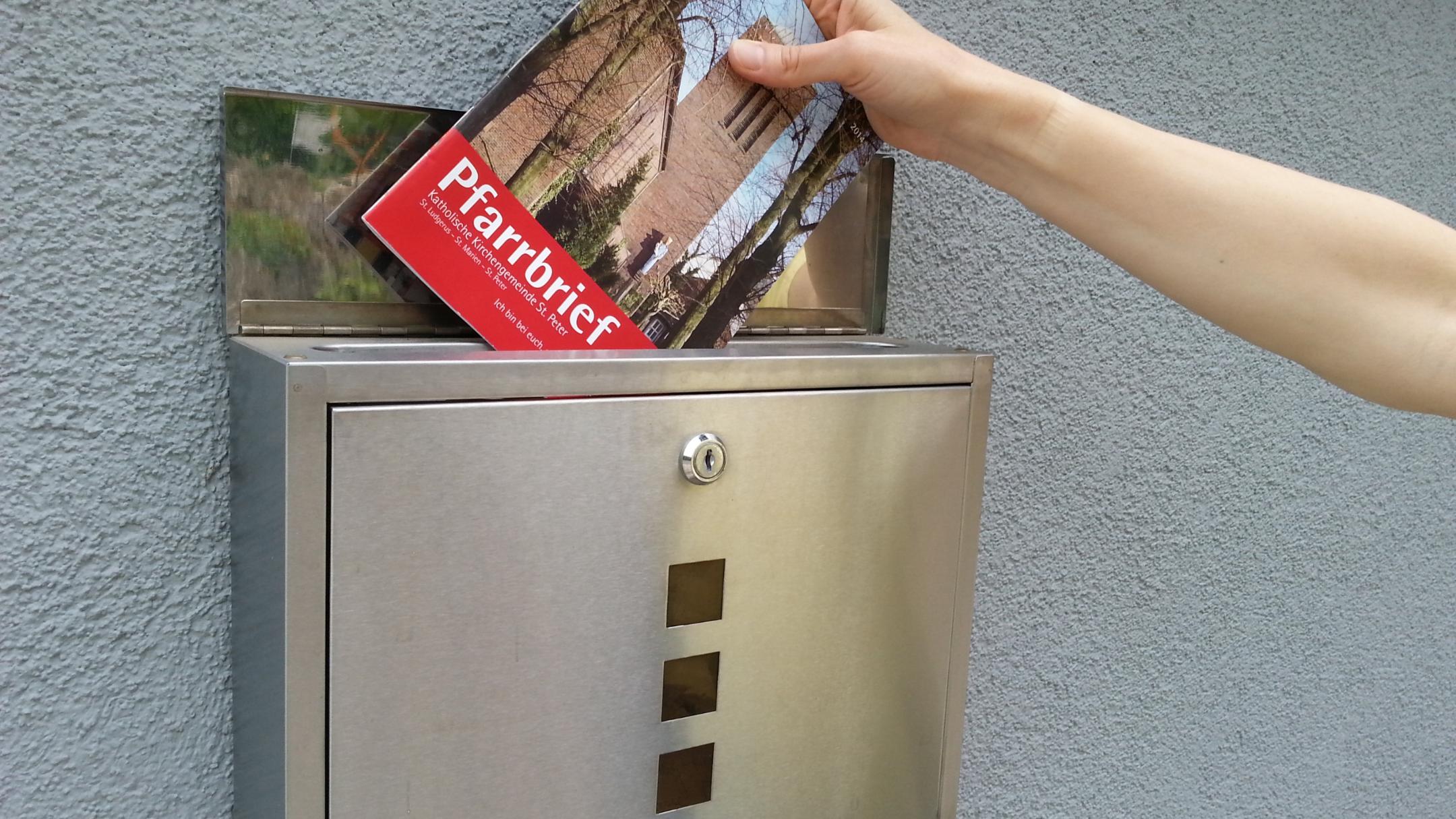 Ein Pfarrbrief wird in einen Briefkasten gesteckt.