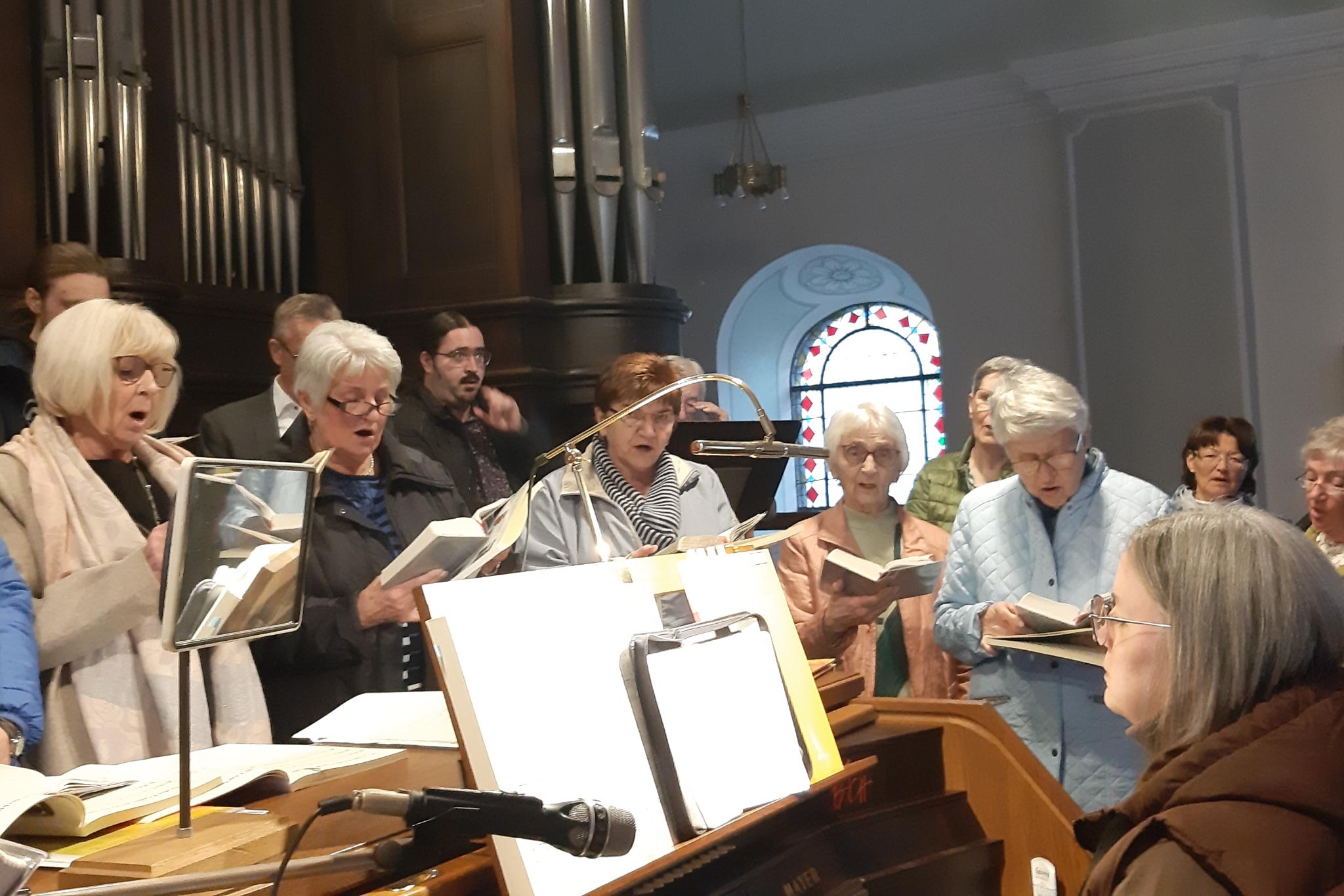 Frauen stehen um eine Organistin auf der Orgelempore und singen